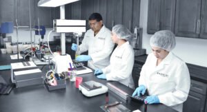 Two lab workers at Radical Cosmetics batching products in a state-of-the-art lab. The photo shows two professionals in white lab coats, safety glasses, and gloves, carefully measuring and mixing cosmetic ingredients. The lab is bright and clean, with stainless steel workstations and clear, labeled containers filled with vibrant, natural-colored ingredients. In the background, various cosmetic production tools and equipment are visible, ensuring the highest standards of quality control and safety. The lab workers are focused on creating innovative, high-performance beauty products, adhering to the Clean Beauty Movement principles. This behind-the-scenes image highlights the precision, science-backed formulations, and ethical manufacturing practices that go into each product, including skincare and cosmetics that are cruelty-free, paraben-free, and made with natural, non-toxic ingredients. Radical Cosmetics ensures sustainable production, using eco-conscious packaging and ethical sourcing of materials.