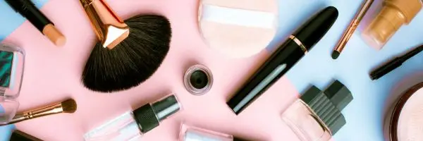 Flat lay of assorted cosmetics, including lipsticks, eyeshadows, and skincare products, arranged aesthetically on a neutral background.
