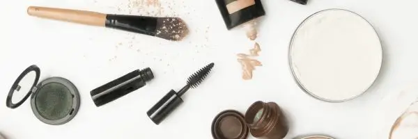 Flat lay of assorted cosmetics, including lipsticks, eyeshadows, and skincare products, arranged aesthetically on a neutral background.